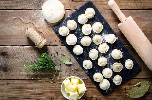 Ingredienti per pelmeni, ravioli, gnocchi - pasta, rosmarino, mattarello, filo di tela, burro, alloro. Vista dall'alto. Sfondo in legno — Foto Stock