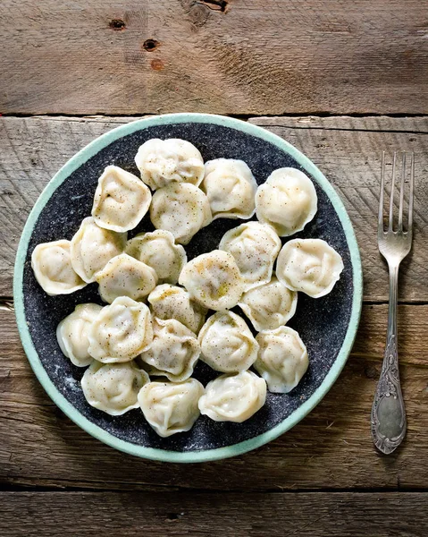 Boiled prepared homemade russian pelmeni, dumplings, ravioli with meat on grey plate with fresh parsley, pepper, wooden rustic background. Top view. Copyspace — Stock Photo, Image