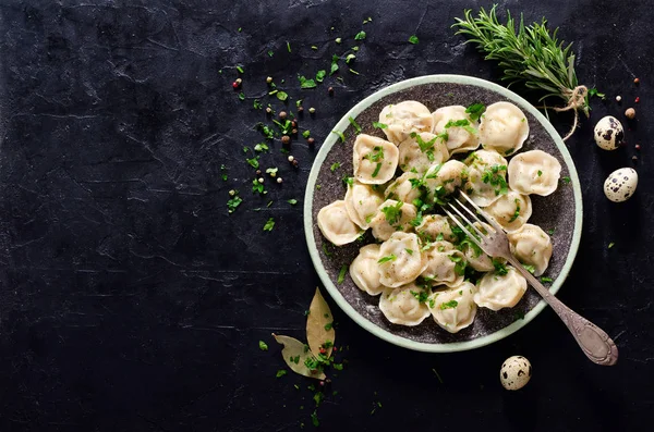 Pelmeni tradizionali russi, ravioli, gnocchi con carne su fondo di cemento nero. Prezzemolo, uova di quaglia, pepe, rosmarino, alloro e spezie. Vista dall'alto. Copyspace . — Foto Stock