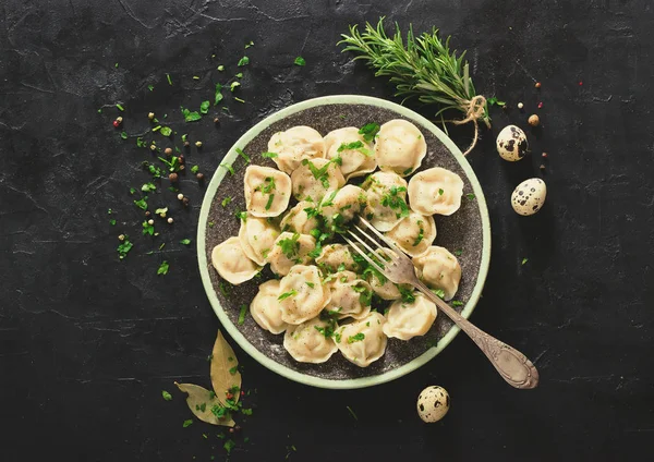 Pelmeni tradizionali russi, ravioli, gnocchi con carne su fondo di cemento nero. Prezzemolo, uova di quaglia, pepe, rosmarino, alloro e spezie. Vista dall'alto. Effetto tonico. Copyspace . — Foto Stock