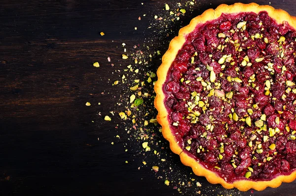 Delicious homamade cranberry, cherry tart with pistachios, powdered sugar on dark wooden background for Christmas. Top view. Handmade with love.