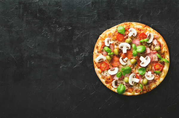 Fresh italian pizza with mushrooms, ham, tomatoes, cheese, olive, basil on black concrete background, rustic table. Copy space. Homemade with love. Fast delivery. Recipe and menu. Top view.
