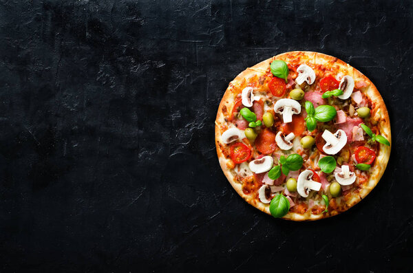 Fresh italian pizza with mushrooms, ham, tomatoes, cheese, olive, basil on black concrete background, rustic table. Copy space. Homemade with love. Fast delivery. Recipe and menu. Top view.