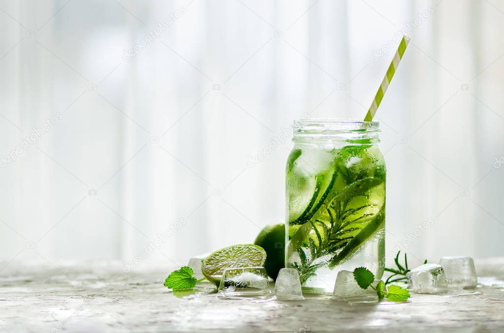 Cold and refreshing detox water with lime, cucumber, rosemary and ice in glass jar. Copyspace.