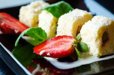 Kivi, şeftali, çilek, nane ile beyaz tatlı rulo. Serverd siyah plaka üzerinde bademli şeftali ve çikolata sos ile.