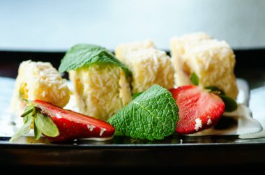 Kivi, şeftali, çilek, nane ile beyaz tatlı rulo. Serverd siyah plaka üzerinde bademli şeftali ve çikolata sos ile.