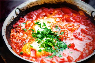 Shakshuka. Geleneksel Yahudi yemeği ve Orta Doğu mutfağı tarifi. Kızarmış yumurta, domates, biber ve maydanoz bir tavada. Yakın, seçici odak. Ev yapımı Kahvaltı