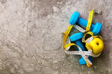 Turkuaz dumbbells ile ölçme bant ve beton zemin üzerine sarı elma. Metniniz için boş alan. Spor kavramı