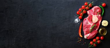 Çiğ taze et biftek domates, acı biber, sarımsak, yağ ve otlar karanlık taş, beton arka plan ile. Afiş.