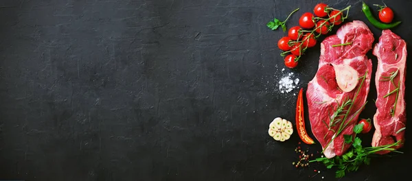 Filetes de carne cruda con tomates cherry, pimiento picante, ajo, aceite y hierbas sobre piedra oscura, fondo de hormigón. Espacio libre para tu texto . — Foto de Stock
