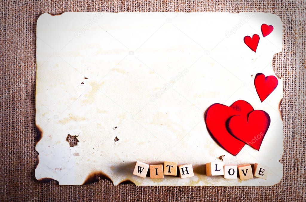 Old vintage sheet of paper, two red hearts, words With love on cubes on burlap, sackcloth background. Retro design effects.