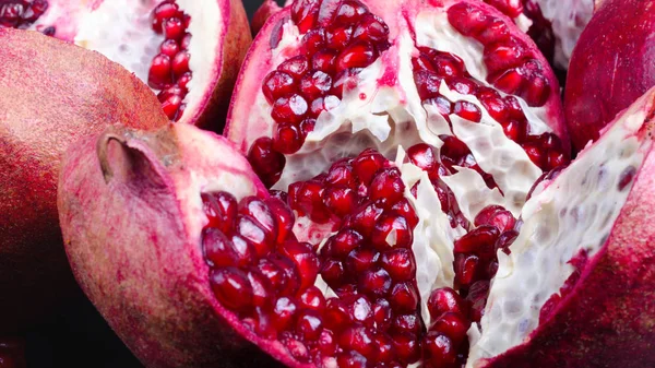Broken pomegranate and grains on black background. Copy space — Stock Photo, Image