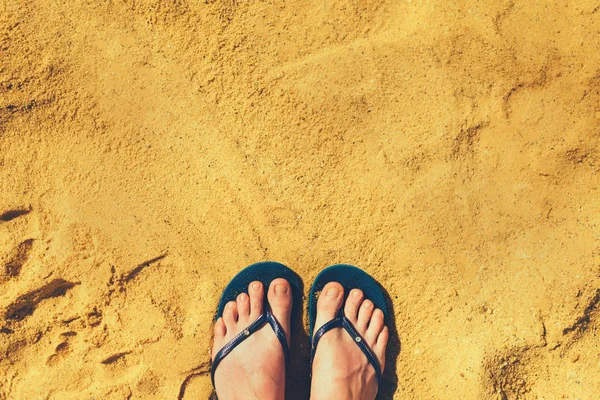 Woman legs in slippers on yellow sand background. Blue flip flops on beach. Copy space, top view. Holiday and travel concept — Stock Photo, Image