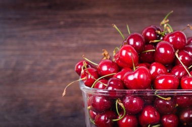 Kopya alanı ile koyu ahşap artalan üzerinde cam kapta tatlı kırmızı kiraz. Yaz ve hasat kavramı. Vegan, vejetaryen, çiğ gıda