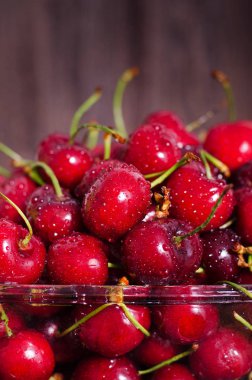 Kopya alanı ile koyu ahşap artalan üzerinde cam kapta tatlı kırmızı kiraz. Yaz ve hasat kavramı. Vegan, vejetaryen, çiğ gıda