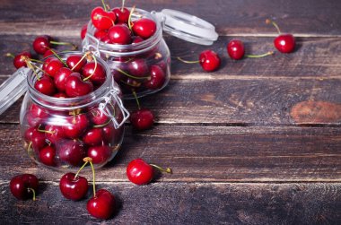 Büyük kırmızı kiraz kopya alanı koyu ahşap zemin üzerine bir cam kavanoza. Yaz ve hasat kavramı. Kiraz makro. Vegan, vejetaryen, çiğ gıda