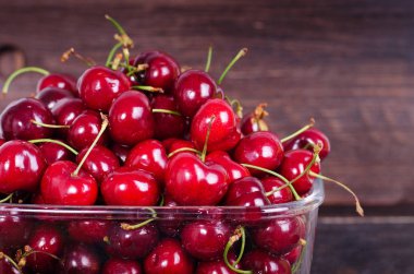 Kopya alanı ile koyu ahşap artalan üzerinde cam kapta tatlı kırmızı kiraz. Yaz ve hasat kavramı. Vegan, vejetaryen, çiğ gıda