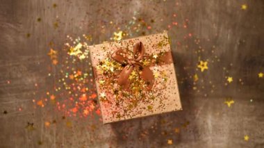Parlak altın yıldızlar, hediye kutusunun üzerinde parıltılı konfeti. Üst Manzara. Noel ve Yeni Yıl dokusu. Satışlar, indirimli fiyat, alışveriş konsepti.