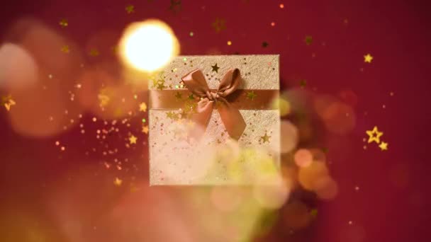 Sparkling gold stars, glitter confetti over gift box on red background. Top view. Christmas and New year texture. Sales, discount price, shopping concept. — 비디오