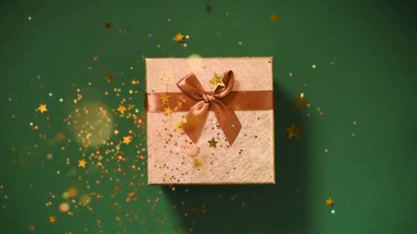 Mousserande guldstjärnor, glitter konfetti över presentförpackning på grön bakgrund. Högst upp. Jul och nyårskonsistens. Försäljning, rabatterat pris, shopping koncept. — Stockvideo