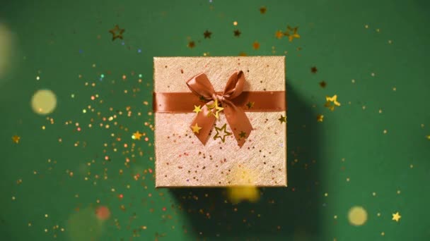 Espumante estrelas de ouro, glitter confetti sobre caixa de presente no fundo verde. Vista superior. Textura de Natal e Ano Novo. Vendas, preço de desconto, conceito de compras . — Vídeo de Stock