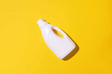 Beyaz plastik temizlik ürünü şişesi, ev kimyasalları ya da sarı arka planda sıvı çamaşır deterjanı. Üst Manzara. Düz yatıyordu. Uzayı kopyala Deterjan şişesi.