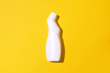 Beyaz plastik temizlik ürünü şişesi, ev kimyasalları ya da sarı arka planda sıvı çamaşır deterjanı. Üst Manzara. Düz yatıyordu. Uzayı kopyala Deterjan şişesi.