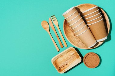 Doğal malzemelerden tek kullanımlık sofra takımı. Bambu tabakları, tahta kaşık, çatal, bıçak, mavi arka planda kağıt bardaklar. Çevre dostu sürdürülebilir yaşam tarzı. Çevre dostu tek kullanımlık aletler
