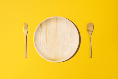 Doğal malzemelerden tek kullanımlık sofra takımı, tahta kaşık, sarı arka planda çatal. Çevre dostu sürdürülebilir yaşam tarzı. Bambu, ahşap ya da kağıt tek kullanımlık sofra takımı kavramı