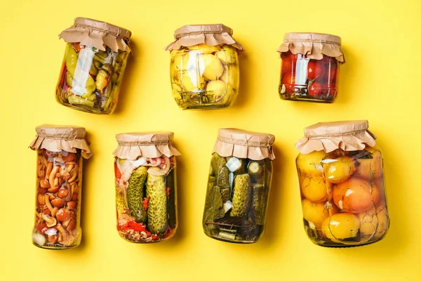 Canned and preserved vegetables in glass jars over yellow background. Top view. Flat lay. Copy space. — Stock Photo, Image