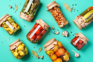Canned and preserved vegetables in glass jars over blue background. Top view. Flat lay. Copy space. clipart