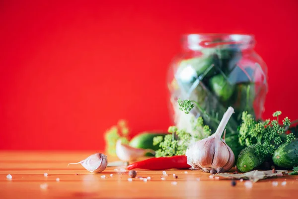 Sottaceto cetrioli in lattine. Ingredienti per cetriolini marinati, barattolo di vetro, aglio, aneto, sale, pepe su fondo rosso. Ricevuto. Concetto di conservazione delle verdure . — Foto Stock