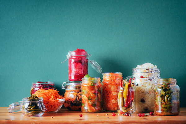 Assortment of various fermented and marinated food over wooden background, copy space. Fermented vegetables, sauerkraut, pepper, garlic, beetroot, korean carrot, cucumber kimchi in glass jars.