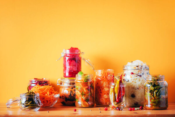 Assortment of various fermented and marinated food over wooden background, copy space. Fermented vegetables, sauerkraut, pepper, garlic, beetroot, korean carrot, cucumber kimchi in glass jars.