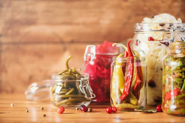 Sortiment různých fermentovaných a marinovaných potravin na dřevěném pozadí, kopírovací prostor. Kvašená zelenina, zelí, pepř, česnek, řepa salátová, korejská mrkev, okurkové kimchi ve skleněných nádobách. — Stock fotografie