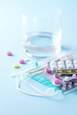 Terapi kavramı, virüs gribinin önlenmesi, virüs saldırısı, grip hapları, antibiyotikler ve vitaminler, mavi arka planda koruyucu yüz maskeleri. Coronavirus Covid-19. Boşluğu kopyala