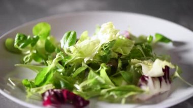 Taş tabağa düşen yeşil salatayı karıştırıyorum. Üst Manzara. Vegan ve çiğ gıda konsepti.