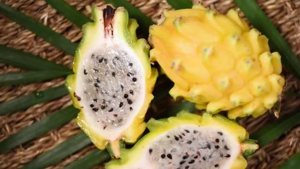 Yellow pitahaya on palm branch, rotating background. Top view. Citrus fruits. Vegan and raw food concept. Sliced dragon fruit texture — Stock Video