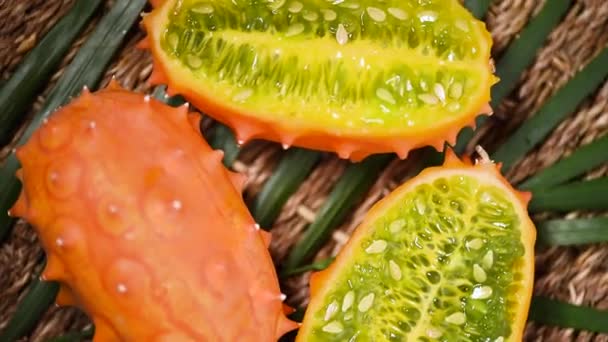 Geschnittene afrikanische gehörnte Melone rotierenden Hintergrund. Ansicht von oben. Exotische Kiwano-Melonenfrüchte, tropischer Palmenzweig. Veganes und Rohkost-Konzept.