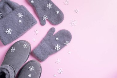 Kış sıcacık kıyafetleri düz. Yünlü kadın kıyafetleri, atkı, botlar, pembe arka planda kar taneleri. Üst görünüm, alanı kopyala
