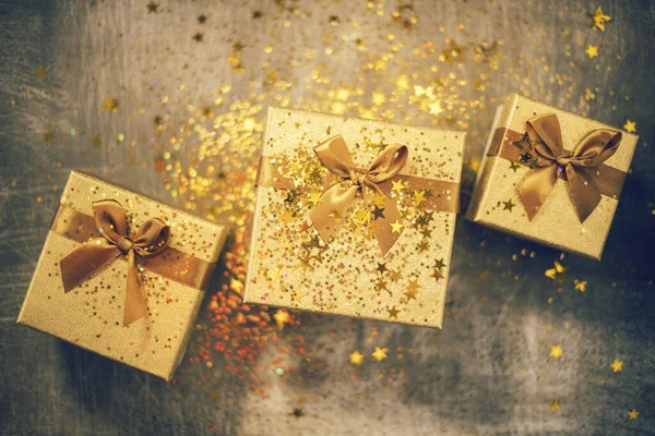 灰色の背景に金色の星と輝きを持つクリスマスギフトボックス。黄金のリボンで結ばれたギフトボックス。トップビュー、コピースペース。休日のコンセプト. — ストック写真