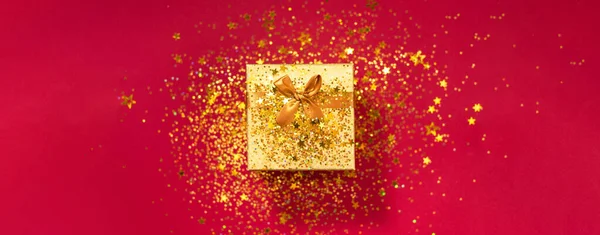 Gift box with sparkling gold glitter on red background. Romantic card. New year, Christmas, Valentines day concept of greetings. Copy text. Top view, flat lay.