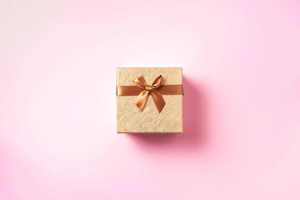 Caja de regalo con brillo dorado brillante sobre fondo rosa. Tarjeta romántica. Nuevo año, la Navidad, el día de San Valentín el concepto de los saludos. Copiar texto. Vista superior, plano . — Foto de Stock