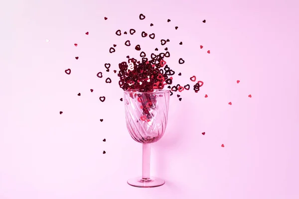 Copo de vinho com coração confetti no fundo rosa. Vista superior. Dia dos Namorados e conceito de amor romântico. Espaço de cópia — Fotografia de Stock