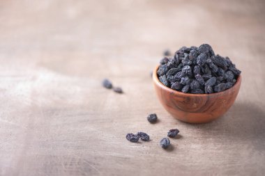 Ahşap desenli arka planda, tahta kasede siyah kuru üzümler. Uzayı kopyala Süper yemek, vejetaryen, vejetaryen gıda konsepti. Taze kuru üzümlü Makro, seçici odaklanma. Sağlıklı çerez