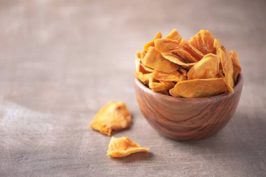 Ahşap desenli arka planda ahşap kasede kurutulmuş mango. Uzayı kopyala Süper yemek, vejetaryen, vejetaryen gıda konsepti. Portakallı kurutulmuş mango dilimleri, seçici odaklanma. Sağlıklı çerez.