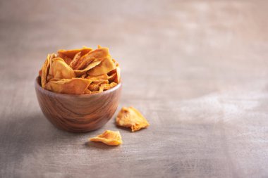 Ahşap desenli arka planda ahşap kasede kurutulmuş mango. Uzayı kopyala Süper yemek, vejetaryen, vejetaryen gıda konsepti. Portakallı kurutulmuş mango dilimleri, seçici odaklanma. Sağlıklı çerez.