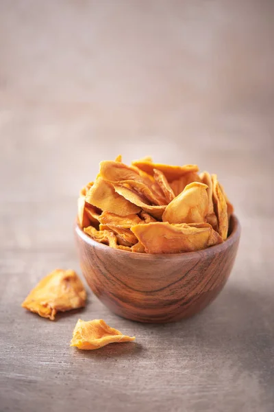 Dried mango in wooden bowl on wood textured background. Copy space. Superfood, vegan, vegetarian food concept. Macro of orange dried mango slices, selective focus. Healthy snack.