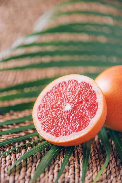 Fresh red grapefruit with palm leaves on rattan background. Copy space. Creative design banner. Tropical travel, exotic fruit. Vegan and vegetarian food. Summer time