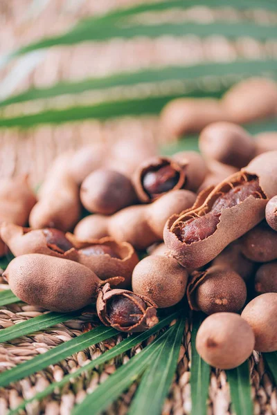 Édes érett tamarind pálmalevéllel a rattan háttéren. Másold a helyet. Trópusi utazás, egzotikus gyümölcs. Vegán és vegetáriánus fogalom — Stock Fotó